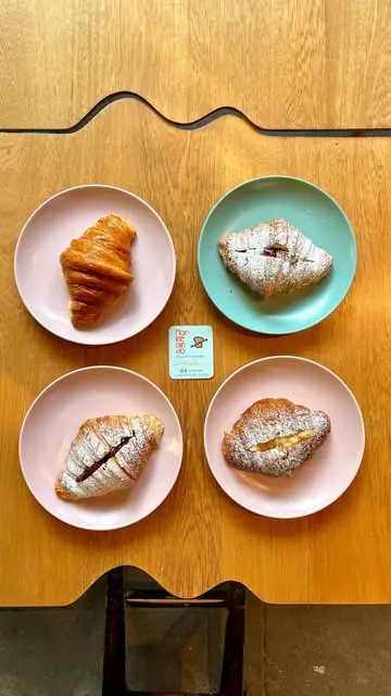 Cuatro croissants en platos de colores sobre una mesa de madera